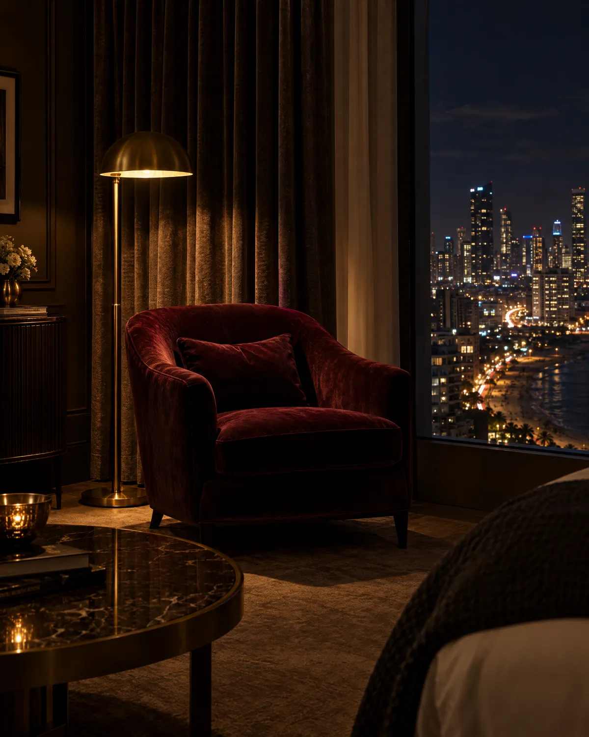 Burgundy velvet armchair and a brass floor lamp by a window over a seaside city at night